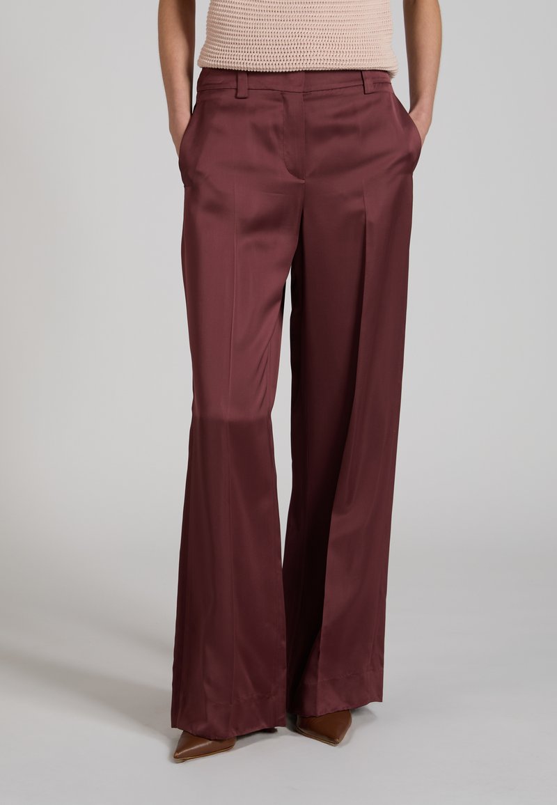 Mujer con pantalones de satén burdeos de pierna ancha con bolsillos, combinados con un top de punto beige y zapatos marrones de punta afilada.