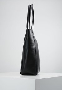 Czarna skórzana torba na ramię z dwoma wydłużonymi uchwytami, zwężanym kształtem, gładką fakturą i minimalistycznym designem bez widocznych elementów metalowych.
