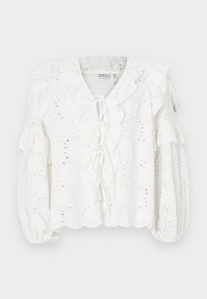 Blusa blanca con tela de ojal, cuello y mangas con volantes. Presenta un cierre de lazo en la parte delantera y un acabado texturizado.