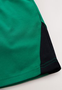 Green cotton fabric shorts with black side accents, featuring a smooth texture and double stitching along the hem for durability.