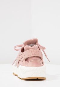 Rosa Nike Air-sneaker med vit sula, bakvy som visar upphöjd "NIKE"-logotyp på hälslanget och snören knutna i en rosett.