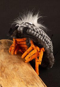 Plush crab toy with gray checked shell, black accents, orange spotted claws, and white faux fur. Positioned near a wooden surface.
