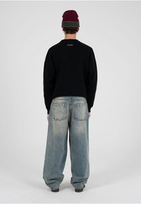 Sudadera negra con hombros caídos y logo bordado en la espalda, combinada con unos vaqueros grandes y desgastados de color azul claro con dos bolsillos traseros.