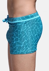 Shorts de bain aqua avec un motif abstrait fluide en bleu clair. Équipés d'une taille élastique avec un lien, fabriqués à partir d'un matériau extensible.