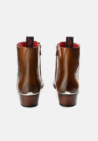 Braune Leder-Stiefeletten mit glatter Textur, seitlichen Reißverschlüssen, schwarzen und roten Zuglaschen sowie einem Holzabsatz.