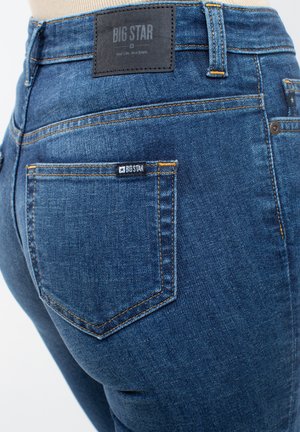 Jeansy Big Star w ciemnoniebieskim dżinsie o gładkiej fakturze. Zawierają pomarańczowe przeszycia, skórzaną naszywkę na plecach oraz małą metkę z logo na kieszeni.