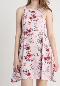 Blumenkleid aus leichtem Stoff. Rosa Grundfarbe mit roten und blauen Blumen. Tailliertes Oberteil, Rüschenträger und ausgestellter Rock. Lässiges Design.