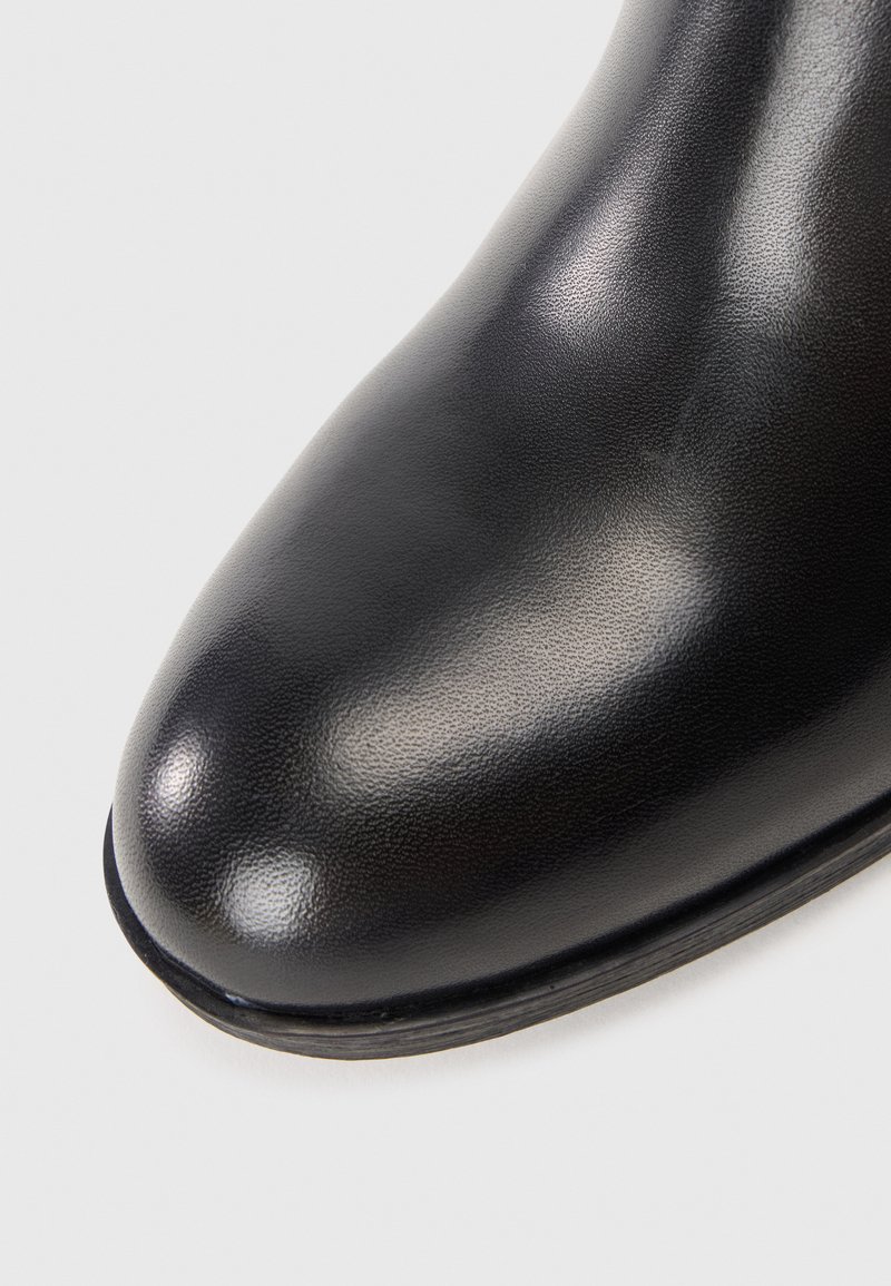 Bottines noires en cuir avec une surface lisse et un bout arrondi, présentant un léger brillant et un design minimaliste, adaptées à un usage formel.