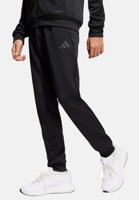 Schwarze Sporthosen mit Slim-Fit, mit eingeprägtem Adidas-Logo, aus strukturiertem Material, kombiniert mit weißen Sneakers.