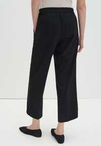 Pantalon noir court avec une ceinture élastique, doté de deux poches arrière, une texture lisse et une coupe droite.