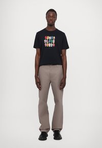 T-shirt en coton noir avec un design graphique coloré de lèvres sur le devant. Assorti à un pantalon beige et des chaussures noires.