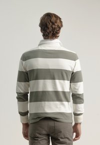 Camisa polo de manga larga con rayas alternas en verde oliva y blanco, cuello, y una textura suave, combinada con pantalones caqui.