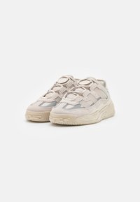 Zapatillas de deporte de color beige claro con una parte superior de tejido texturizado, acentos grises, suela gruesa y diseño de cordones con ojales reforzados.