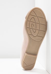 Semelle d'une chaussure plate beige avec une semelle extérieure en caoutchouc antidérapante à motif, taille 37, reposant à la verticale contre un mur blanc.