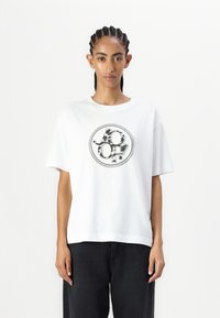 White cotton t-shirt featuring a round black and leopard print logo, short sleeves, slightly loose fit, and a crew neck design.