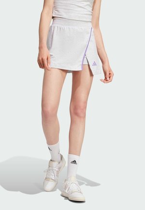 Grijze sportrok met een paarse rand, gemaakt van zacht materiaal, beschikt over een zij-split ontwerp, gecombineerd met witte sokken en schoenen.