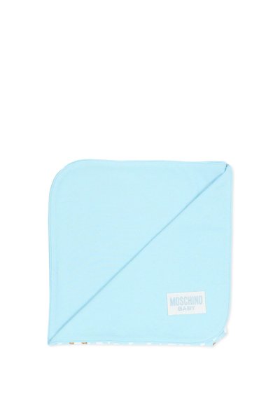 Jasnoniebieski kocyk dziecięcy złożony na ukos, ukazujący gładką tkaninę oraz metkę "Moschino Baby" w prawym dolnym rogu.