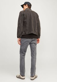 Black denim jacket with a relaxed fit, gray jeans, and light-colored sneakers. The jacket has a classic collar and side pockets.