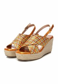 Sandalias de cuña con tiras trenzadas multicolores en rojo, naranja y azul, con un tacón brillante en bronce y una plataforma de yute natural.
