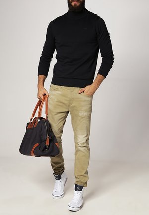 Czarny sweter z golfem, beżowe przetarte dżinsy, białe wysokie trampki oraz duża czarna torba z brązowymi akcentami. Prezentacja codziennego stroju.