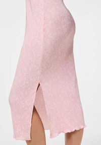 Ribana obleka do kolen v roza barvi z belim cvetličnim vzorcem, ki ima stranski razporek in valovito rob za dodano teksturo in podrobnosti.