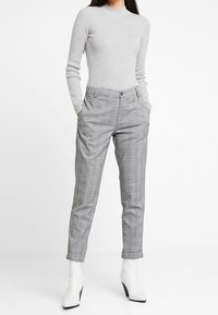 Szary prążkowany top z długim rękawem w połączeniu z szarymi spodniami w kratę o dopasowanym kroju i delikatnymi kieszeniami, uzupełniony białymi botkami za kostkę.