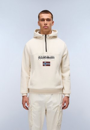 Beige hoodie met een rits aan de voorkant, voorzien van een logo en een vlagpatch. Effen textuur, losse pasvorm, gecombineerd met lichtbeige cargo pants.