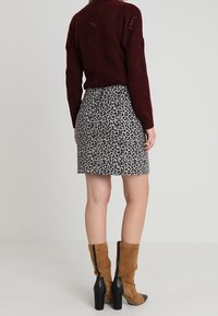 Jersey burdeos combinado con una falda gris con estampado de leopardo, botas marrones hasta la rodilla con detalles en negro, diseño ajustado, tejido texturizado.