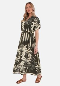 Robe maxi vert foncé avec motif de feuilles de palmier blanches. Fluide, manches courtes, devant boutonné et ceinture à nouer pour un ajustement personnalisé. Sandales marron.