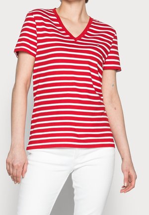 Personne portant un t-shirt à manches courtes rayé horizontalement rouge et blanc à col en V et un pantalon blanc, debout les bras détendus.