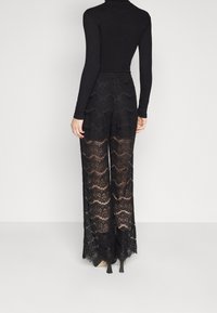 Zwarte kanten wijde broek met een golvend patroon, transparante textuur en contrasterende voering. Gestyled met een aansluitende zwarte langemouwen top.