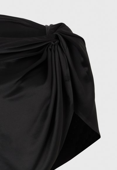 Μαύρο σατέν ύφασμα, μαζεμένο και δεμένο σε μια γωνία, δημιουργώντας απαλά πτυχώσεις και ρίγος επάνω σε ένα απλό ανοιχτό φόντο.