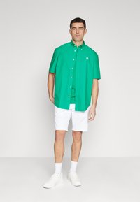 Grøn kortærmet skjorte med knapper og krave, parret med hvide shorts og hvide sneakers. Glat stof, enkel design og logo detalje på skjorten.