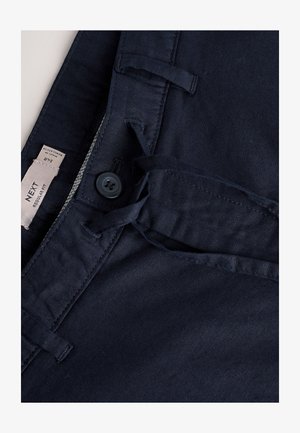 Tumedate sinised puuvillased püksid, millel on nööp-kinnitus, pael ja taskute detailid. Sile tekstuur ja tavapärase lõikega disain. Silt on nähtav.