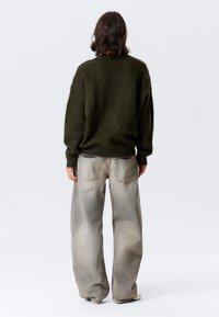 Pulover supradimensionat verde închis, pufos, tricotat, cu umeri căzuți, asortat cu blugi deschiși la culoare, largi și decolorați, cu buzunare în spate.