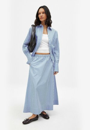 Set aus blau-weiß gestreifeter Bluse und langem Rock, aus Baumwollstoff, entspannte Passform, kombiniert mit einer schwarzen Tasche und braunen Ballerinas.