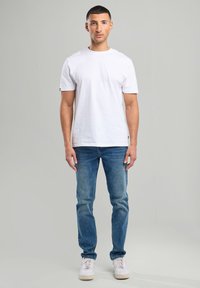 White cotton t-shirt with short sleeves, paired with blue denim jeans and white sneakers. Simple, fitted design with no visible patterns.