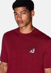 Bordeaux t-shirt met korte mouwen van katoen, met een blauw en wit logo op de borst, een ronde hals en een gladde textuur.