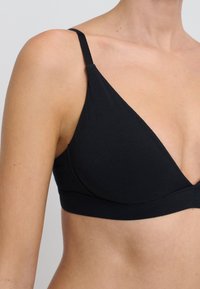 Bralette nera a forma di triangolo con spalline sottili e regolabili, tessuto morbido, design senza cuciture e un'ampia fascia sotto il seno. Senza imbottitura o ferretto visibile.