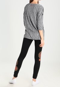 Šedý, převeliký top s tříčtvrtečními rukávy; spárovaný s černými legínami s červenou květinovou výšivkou na kotnících a bílými teniskami.