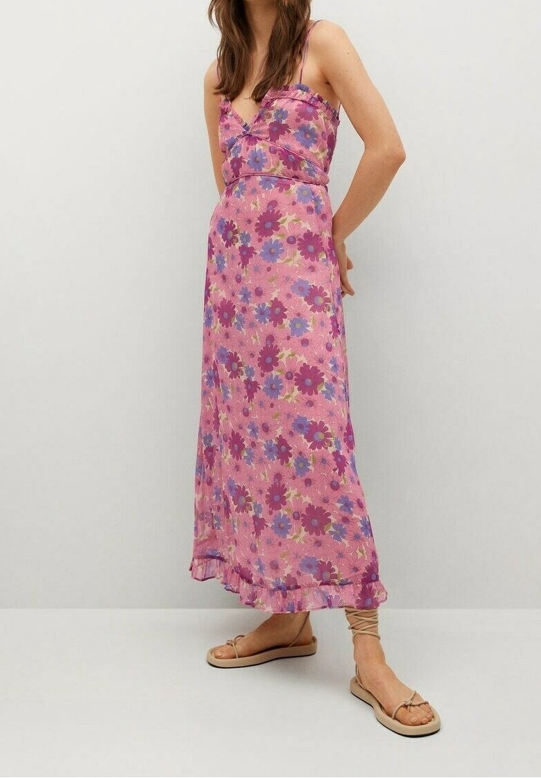 Femme portant une robe maxi rose à fleurs avec des bretelles spaghetti et des sandales beiges à lacets, debout devant un fond blanc uni.