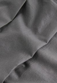 Tissu gris foncé lisse avec des plis doux et une texture subtile visible en gros plan.