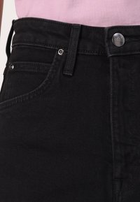 Svarte denimjeans med høy midje, med sølvfarget knapplukking, beltehemper og subtile sømdetaljer langs lommene.