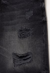 Tissu en denim noir présentant trois zones usées avec des détails de déchirure et d'effilochage visibles. La texture semble usée et légèrement décolorée.