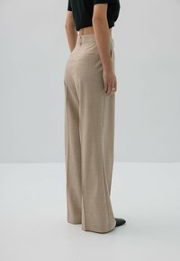 Beżowe spodnie o szerokich nogawkach wykonane z fakturowanej tkaniny, z dwoma tylnymi kieszeniami i wysokim stanem, w połączeniu z czarnymi butami.
