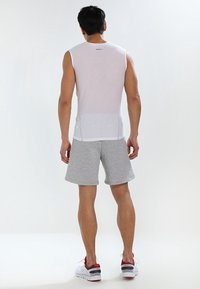 Top atletico bianco senza maniche in rete, abbinato a pantaloncini grigi con vita elastica e texture a coste, indossato con scarpe da ginnastica rosse e nere.