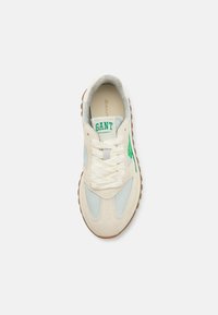 Pantofii sport au un superior din suede crem, accente de albastru deschis, sireturi albe și un logo verde. Dispun de o talpă din cauciuc texturat pentru aderență.