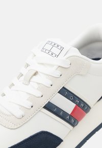 Weiße Sneaker mit marineblauen und roten Akzenten, aus Wildleder und Leder, mit Schnürdesign und einem Logopatch auf der Zunge.