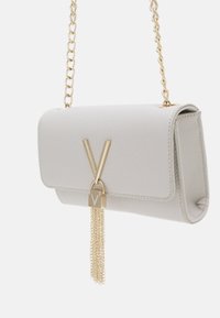 Piccola borsa a tracolla in pelle bianca con una texture, dotata di una catena dorata, che presenta una chiusura a forma di "V" dorata e un dettaglio a frangia.