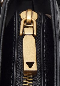 Černý zip se zlatým táhlem ve tvaru trojúhelníku, připevněný na část texturované látky.